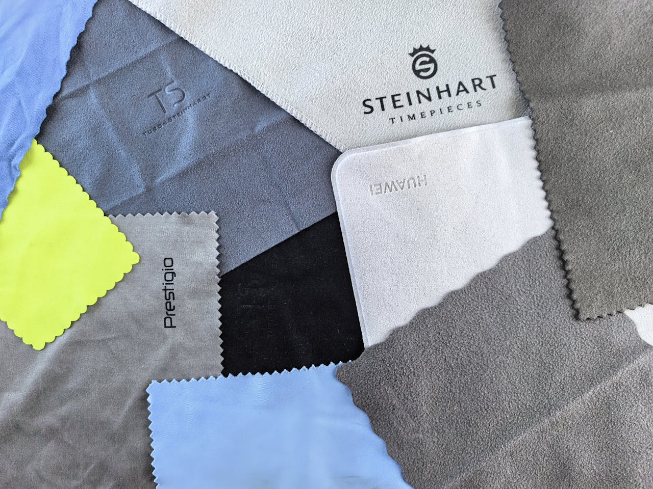 A vibrant flatlay of various cleaning cloths featuring watch brand logos on textured fabrics.